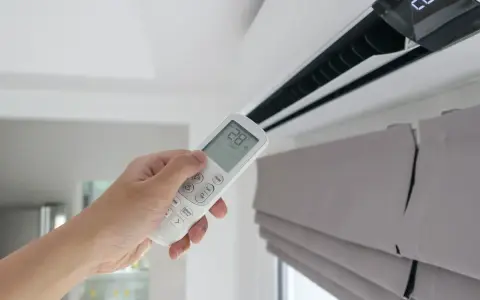 Mano sujetando control remoto de aire acondicionado, mostrando la diferencia entre climatizador y aire acondicionado.