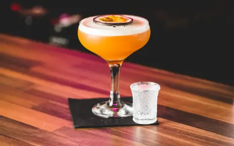 Orzeźwiający passion fruit martini z pianką i plasterkiem owocu, obok kieliszek wody gazowanej. Idealny na letnie wieczory.