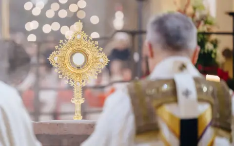 Goldene Monstranz mit Hostie im Schein von Kerzenlicht. Ein Priester in festlicher Kleidung feiert die Messe, ein Moment des weihnachtlichen Christentums.