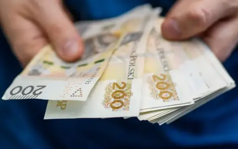 Dłonie trzymają stos banknotów 200 zł. Pieniądze mogą posłużyć do zapłaty czynszu administracyjnego.
