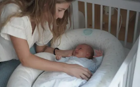Madre observa a su bebé recién nacido, listo para sus siestas. El pequeño sonríe en su nido acogedor.