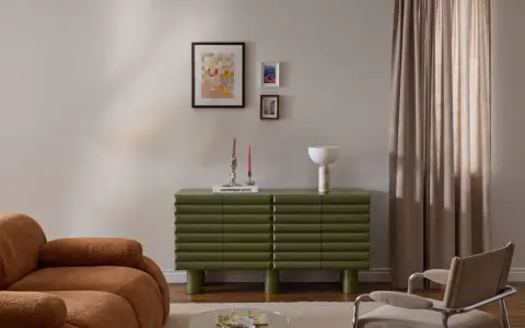 Un salotto moderno con divano color caramello, un mobile verde a coste e un gruppo di quadri appesi in modo originale.