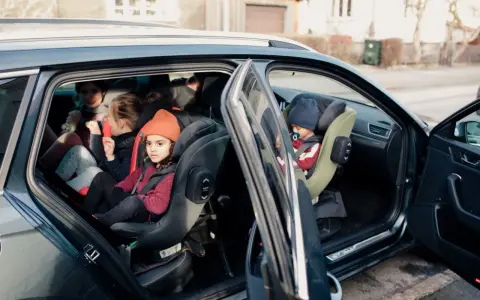 Niños en asientos de coche, uno con gorro naranja. Guía visual para como colocar silla grupo 2 3 sin isofix.