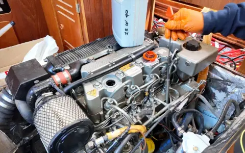 Main d'une personne en gant orange vérifiant le niveau d'huile d'un moteur 4 temps ne démarre pas. Bidon d'huile 25W40 à proximité.