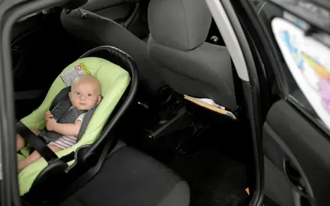 Niemowlę w foteliku na tylnym siedzeniu samochodu. Brak fotelika grozi mandatem.