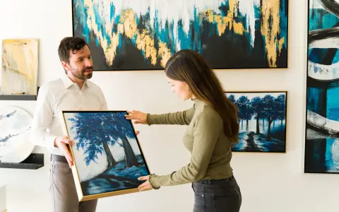 A man and woman admire a painting of blue trees at an art exhibition.