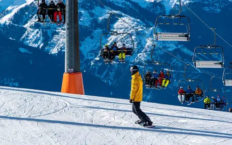 Snowboarder na stoku pod kolejką linową z narciarzami.