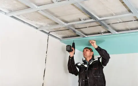 Obrero coloca pladur en techo con taladro.