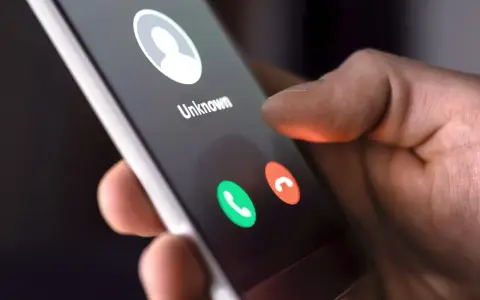Dłoń trzyma smartfon z ekranem połączenia przychodzącego od nieznanego numeru. Dowiedz się, jak dzwonić z zagranicy do Polski na komórkę.