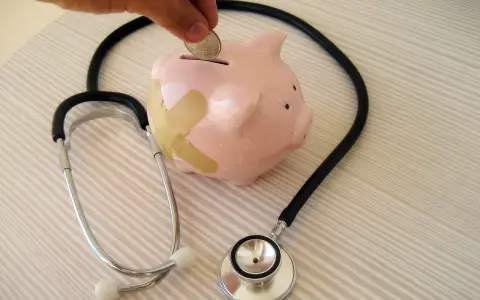 Salvadanaio a forma di maialino con cerotti, uno stetoscopio e una mano che inserisce una moneta. Simboleggia il dottore stipendio e la cura delle finanze.