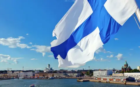 Flaga z niebieskim krzyżem powiewa nad portem w Helsinkach. W tle widać katedrę i inne budynki.