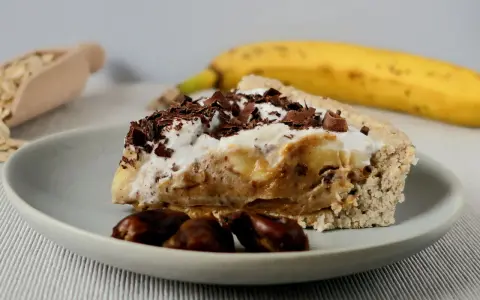 Pyszny sernik banoffee z bananami, karmelem i bitą śmietaną, posypany czekoladą. Obok leży dojrzały banan.