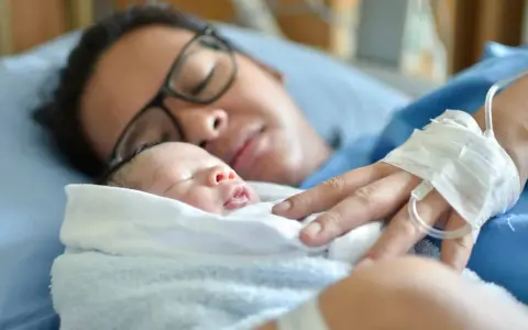 Mutter mit Neugeborenem im Arm, die sich von der Geburt erholt. Die Frage "Wochenfluss wie lange" beschäftigt viele Frauen nach der Entbindung.