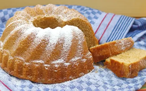 Puszysta babka z cukrem pudrem, obok niej kromki ciasta, na niebieskim ręczniku.