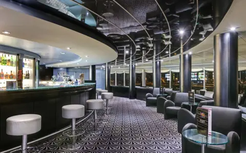 A modern bar with a curved counter, stools, lounge seating, and a patterned carpet.