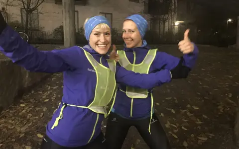 Två glada löpare i blå jackor och reflexvästar ger tummen upp, redo för ett maraton.