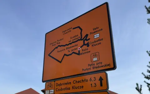 Pomarańczowa tablica z mapą szlaków rowerowych Velo Przemsza. Wskazuje drogę do Pustyni Błędowskiej, Czubatki Klucze i innych miejsc.