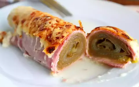 Endive au jambon gratinée, enroulée et coupée en deux, servie sur une assiette blanche avec une sauce crémeuse.