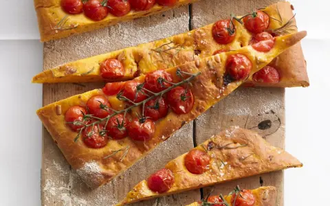 Saftige focaccia mit tomaten und Rosmarin, auf einem Holzbrett mit Mehl bestäubt.