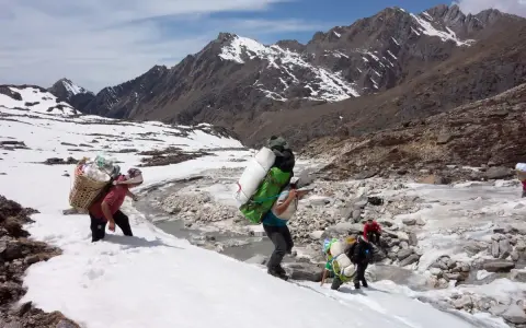 Ludzie niosący ciężkie ładunki w śniegu, zbliżając się do mount everest base camp. Góry w tle.