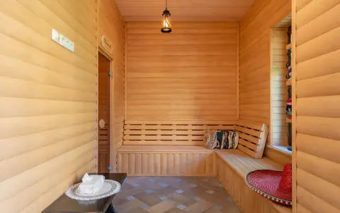 Interior de madera con bancos para relajarse, mostrando varios tipos de saunas. Un sombrero rojo y cojines decoran el espacio.