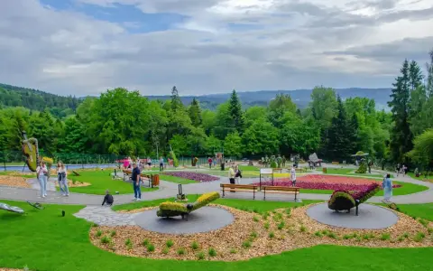 Kolorowy park z rzeźbami z kwiatów i zieleni. Widać ludzi spacerujących alejkami. Sprawdź góra parkowa cennik, by zaplanować wizytę.