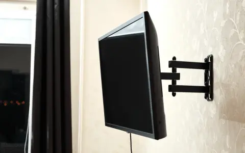 Czarny uchwyt telewizyjny na ścianie, z kablem TV. Idealna wysokość dla komfortowego oglądania.