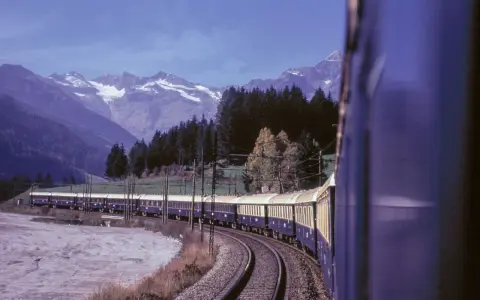 Der Istanbul Express fährt durch eine malerische Berglandschaft mit schneebedeckten Gipfeln und dichten Wäldern.
