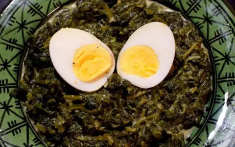 Un plat d'épinards à la crème, parsemé de deux moitiés d'œufs durs, sur une assiette verte décorée.
