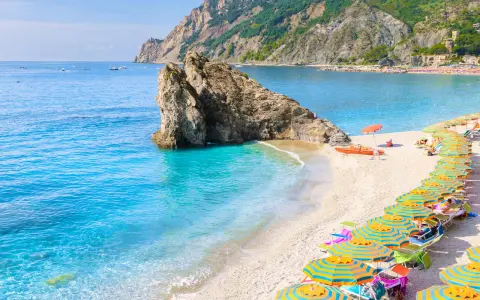 Ein malerischer italien strand mit türkisfarbenem Wasser, einem Felsen im Meer und vielen bunten Sonnenschirmen.