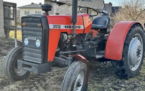 Czerwony ciągnik Ursus 3512 z czarną maskownicą i siedzeniem, stojący na ziemi.
