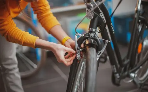 Osoba w żółtym swetrze dokonuje wymiany klocków w rowerze, dbając o sprawne hamulce.