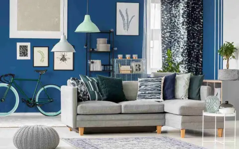 Un soggiorno moderno con divano grigio, pouf e tappeto, dominato da **colori freddi** come il blu intenso delle pareti e i toni verdi e blu degli accessori.