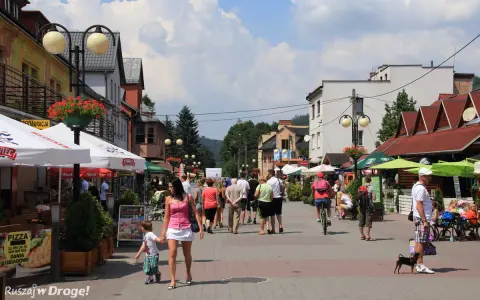 Tętniąca życiem ulica w Wiśle, pełna ludzi spacerujących, rowerzystów i psów. Wiele kawiarni i restauracji oferuje swoje atrakcje.
