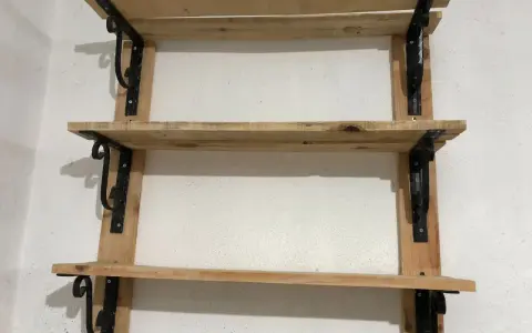 Scaffali fai da te garage: tre ripiani in legno grezzo, fissati a parete con staffe nere decorative. Perfetti per organizzare attrezzi e materiali.