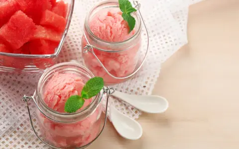 Erfrischendes Wassermelonen-Eis in Gläsern, garniert mit Minze. Daneben ein Schälchen mit frischen Wassermelonenstücken.
