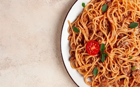 Pyszne spaghetti z mięsem mielonym, udekorowane pomidorkiem i listkami bazylii. Idealne na szybki obiad.