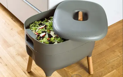 Compostador gris con restos de comida y hojas. Aprende como hacer compost para un jardín sostenible.