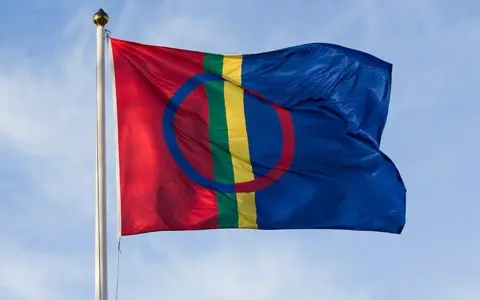 Samiska flaggan vajar stolt mot en blå himmel, en symbol för samiska nationaldagen och ett folk med djupa rötter.