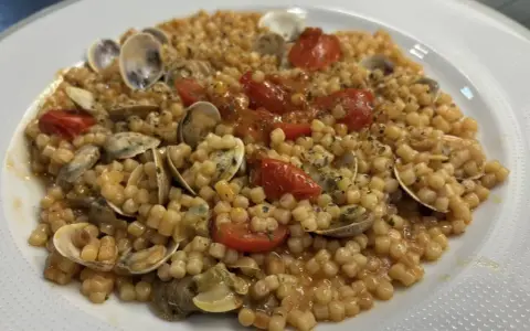 Un piatto invitante di fregola con vongole, pomodorini e prezzemolo, pronto per essere gustato.