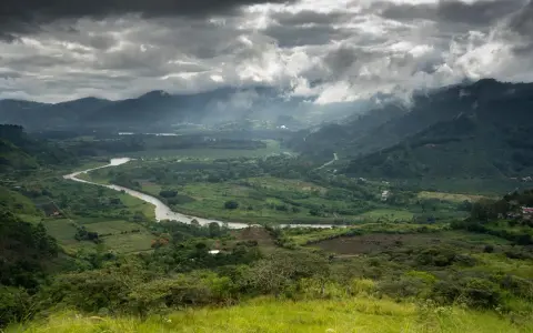 Ein gewundener Fluss schlängelt sich durch ein grünes Tal in Costa Rica. Wolken ziehen über die Berge, die das Bild umrahmen.