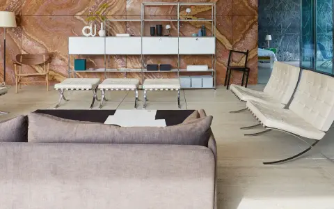 Soggiorno moderno con divano grigio, poltrone in pelle bianca e sgabelli, su sfondo di travertino rosso. Il **case design** è elegante e funzionale.