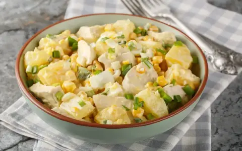 Una ciotola piena di insalata di pollo e patate, con mais, uova sode e cipollotto fresco.