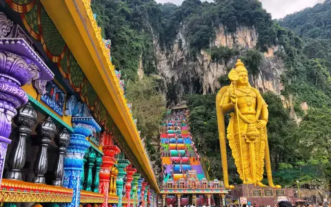 Kolorowe schody Batu Caves w Malezji, prowadzące do jaskini, obok złotej statuy boga Murugana. Warto zobaczyć!