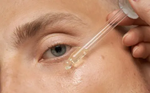 Nahaufnahme eines Auges, auf das ein Tropfen Öl aus einer Pipette aufgetragen wird.