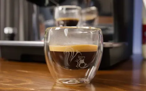 Ein dampfender doppio macchiato in einem doppelwandigen Glas mit einem Eichhörnchen-Motiv.