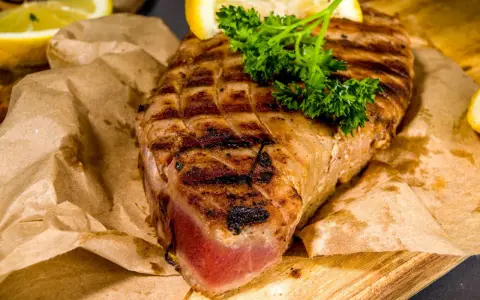 Saftiges Thunfischsteak, perfekt gegrillt, mit Zitronenspalten und Petersilie garniert, auf Packpapier serviert.