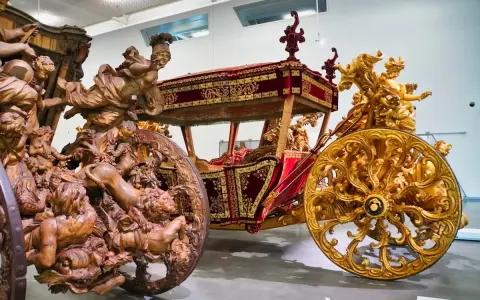 Prunkvolle Kutschen im Kutschenmuseum Lissabon: Eine aus Holz geschnitzte, die andere golden verziert, beide mit aufwendigen Figuren.