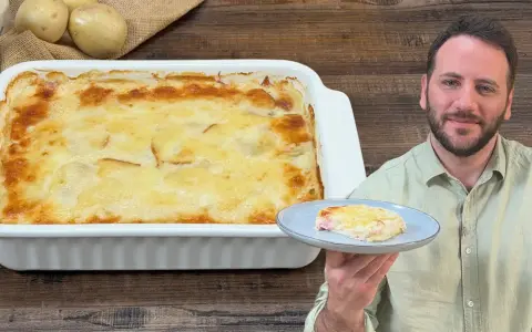 Un uomo sorride mostrando una fetta di parmigiana di patate appena sfornata, dorata e filante.
