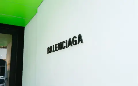 Il logo Balenciaga su una parete bianca, sotto un soffitto verde brillante. Chi è Balenciaga? Un nome che evoca alta moda e design audace.